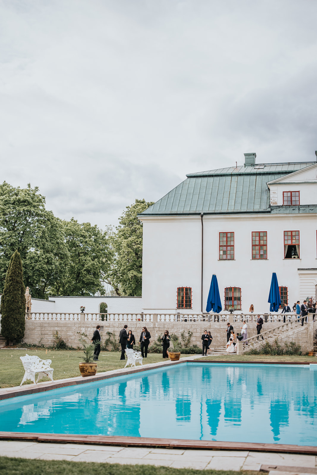 Fotografi taget på bröllopsgästerna som går tillsammans från Häringe slott, längs poolen påväg till middagen